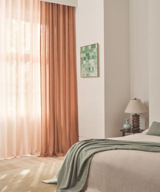 Light pink sheer drapes with neutral bed with lien green throw and bedside table with quirky light