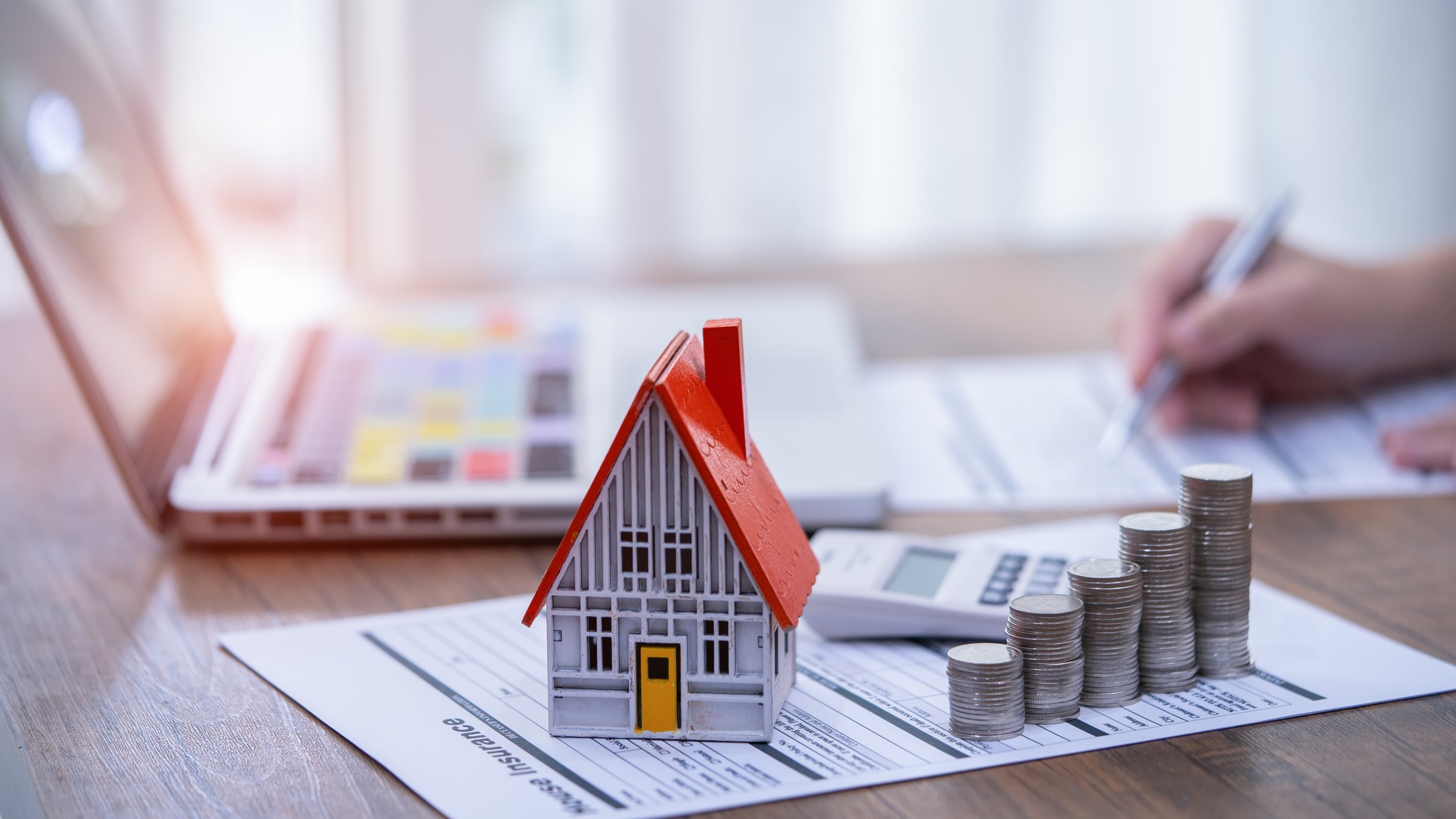 a model house, calculator and stack of coins sitting on a mortgage application