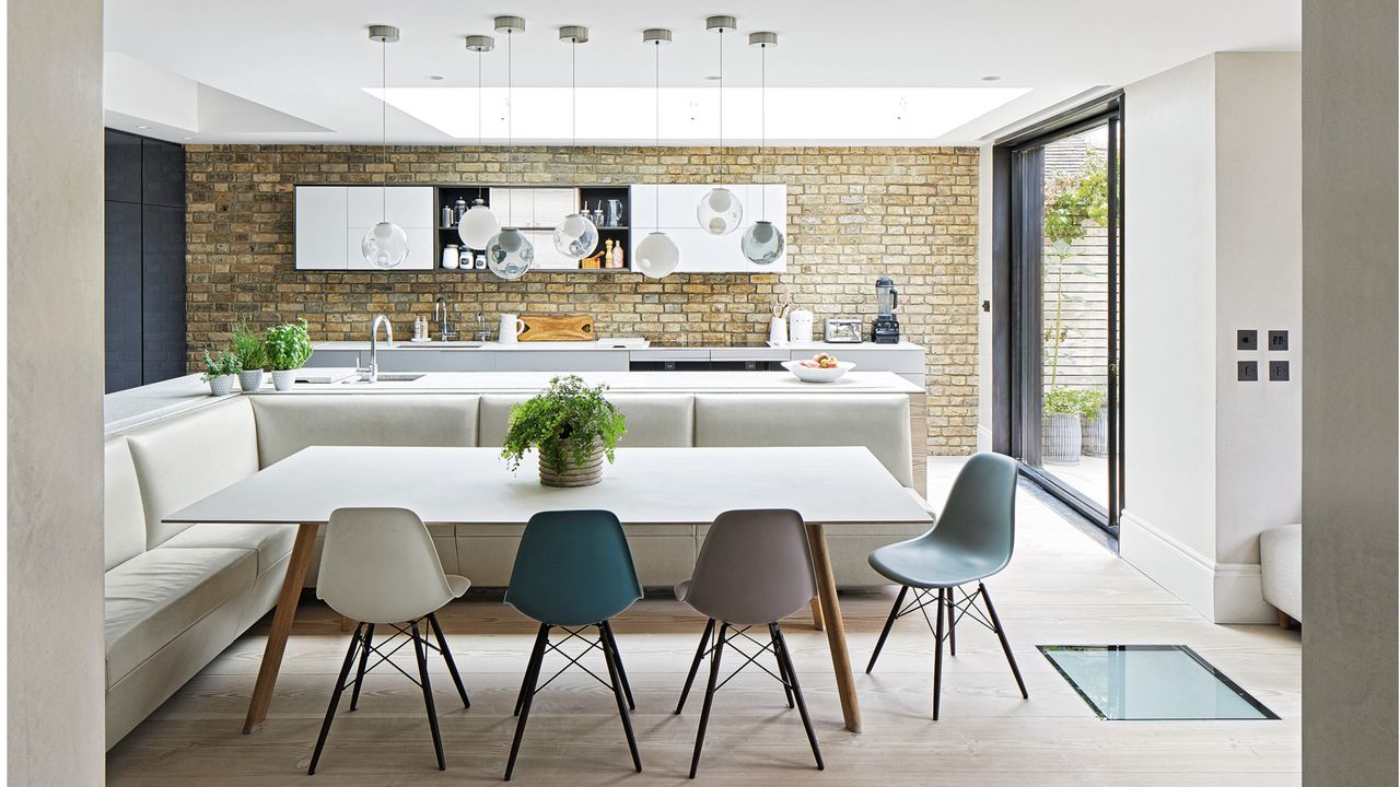 kitchen diner with pale leather bench seating, white dining table with coloured chairs and French door out to the garden