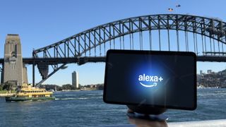 An Amazon Echo smart display with an Alexa Plus graphic posed in front of the Sydney Harbour Bridge