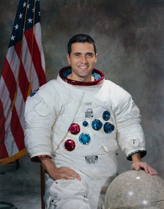 Astronaut Harrison H. Schmitt poses for his portrait smiling with his left hand on a globe.