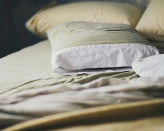 a close up shot of a neutral colored bed with pillows of the same color palette strewn across it haphazardly