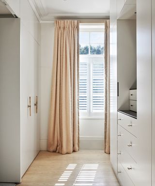 Dressing area with white built in wardrobes and pale wooden floor.