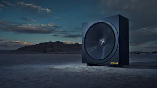 A promotional photo of the Deus Invicta 60 subwoofer on a dried lake bed underneath a late evening sky