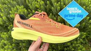 Merrell Morphlite Trail Running Shoes in orange shown in a user's hand with a green plant background