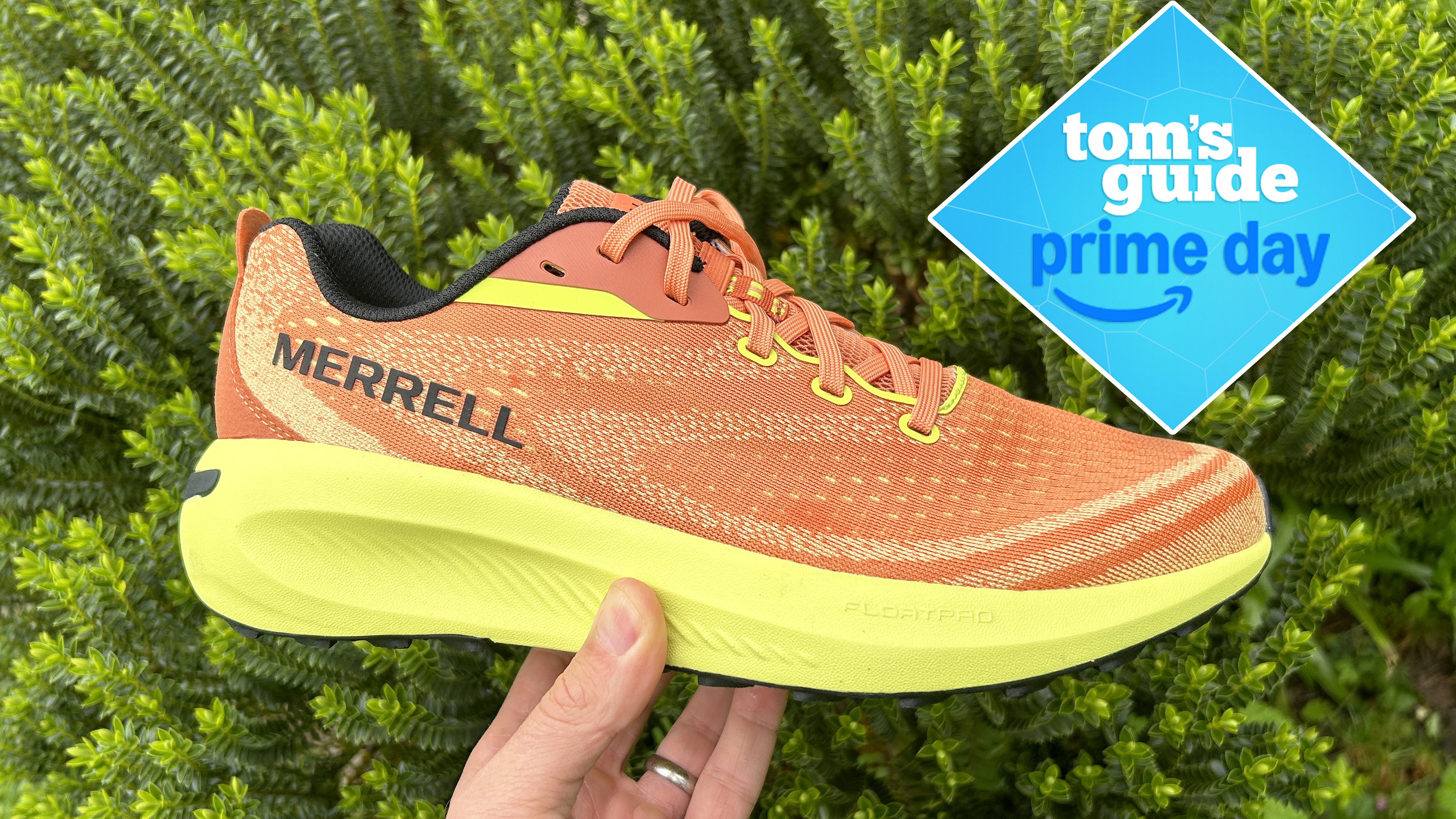 Merrell Morphlite Trail Running Shoes in orange shown in a user&#039;s hand with a green plant background 