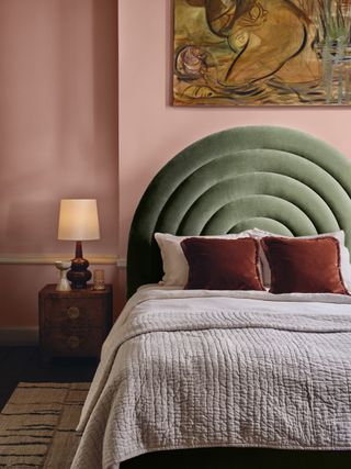 A pink bedroom with green velvet headboard and pale pink quilt