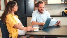 A pregnant couple sit at their dining table to discuss finances.