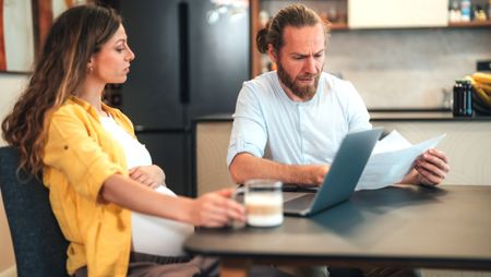 A pregnant couple sit at their dining table to discuss finances.