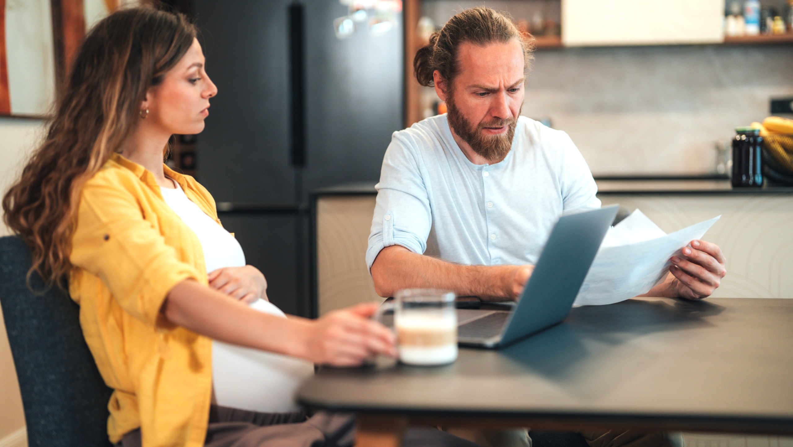 A pregnant couple sit at their dining table to discuss finances.