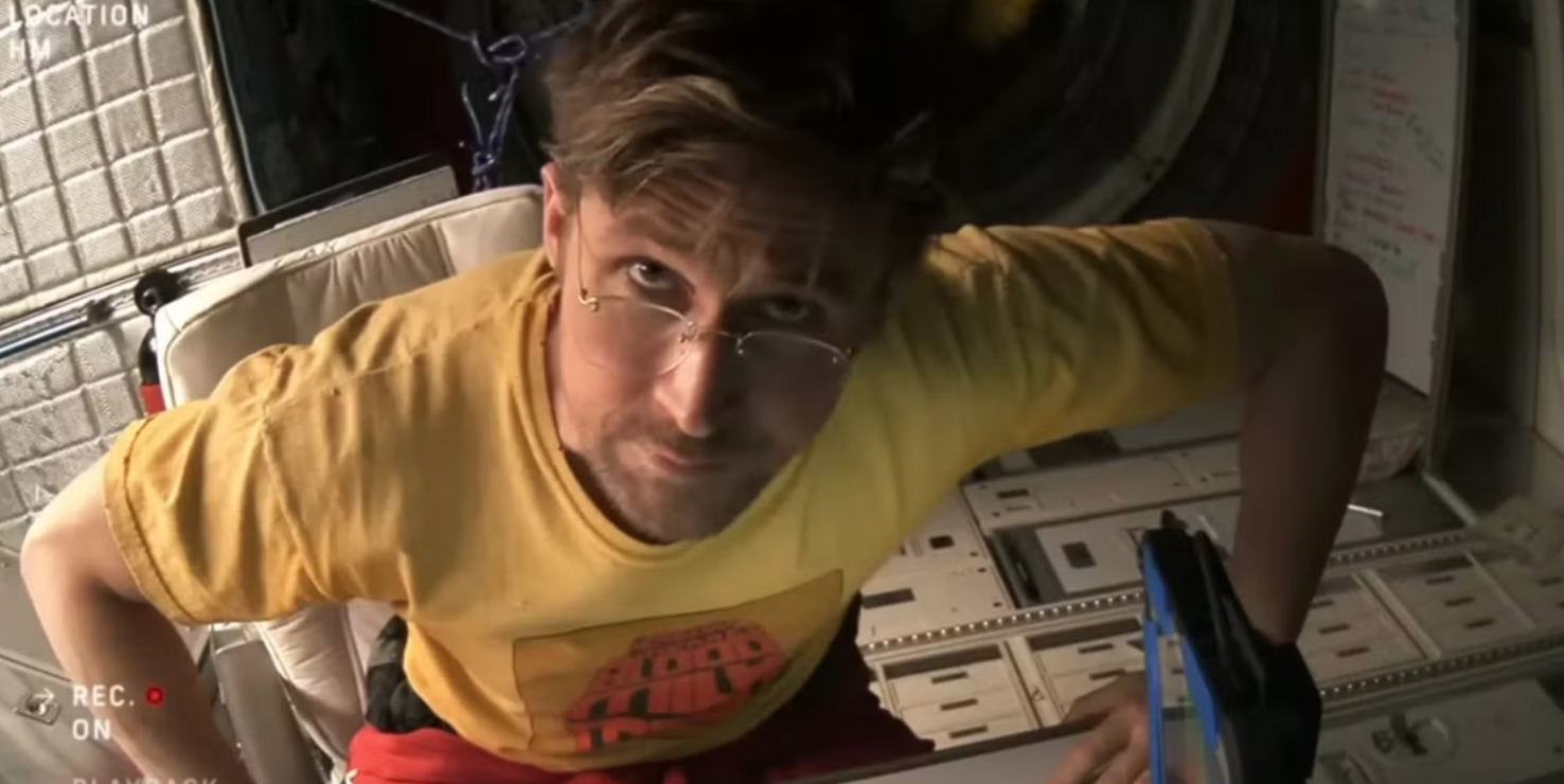 an astronaut in a yellow t-shirt stares into a camera