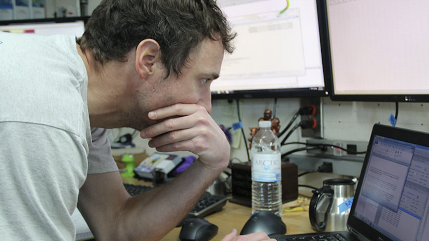 A man leans over a laptop and looks at the screen