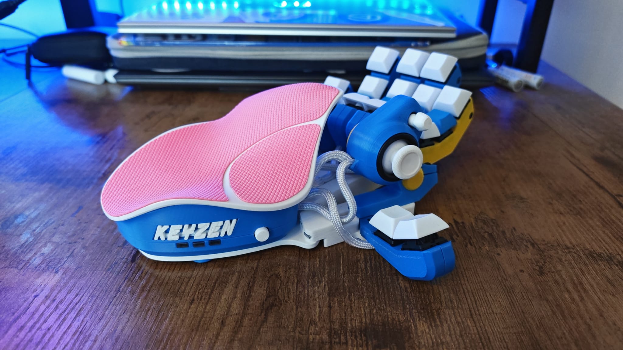 A blue, white, and yellow Azeron Keyzen with pink palm rest tape on a desk