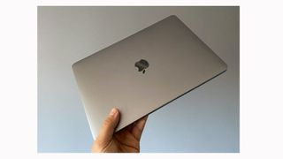 Image shows a hand holding a MacBook Pro M1 from the top.