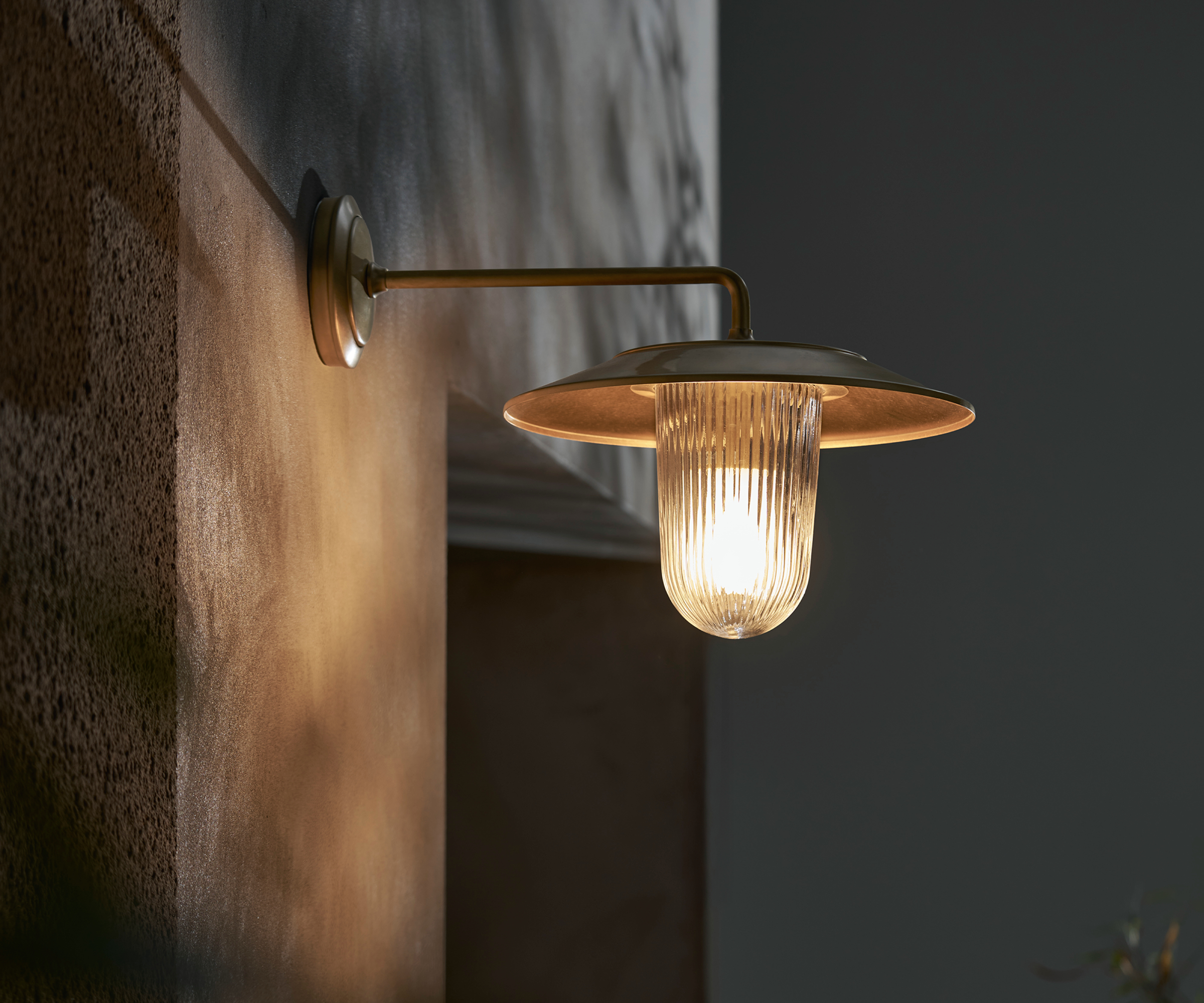 elegant metal porch wall light with ribbed glass fitting below metal shade casting a warm temperature light