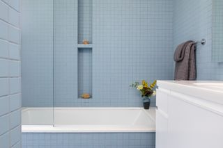 A blue mosaic tiled bathroom with white tub and shower niches