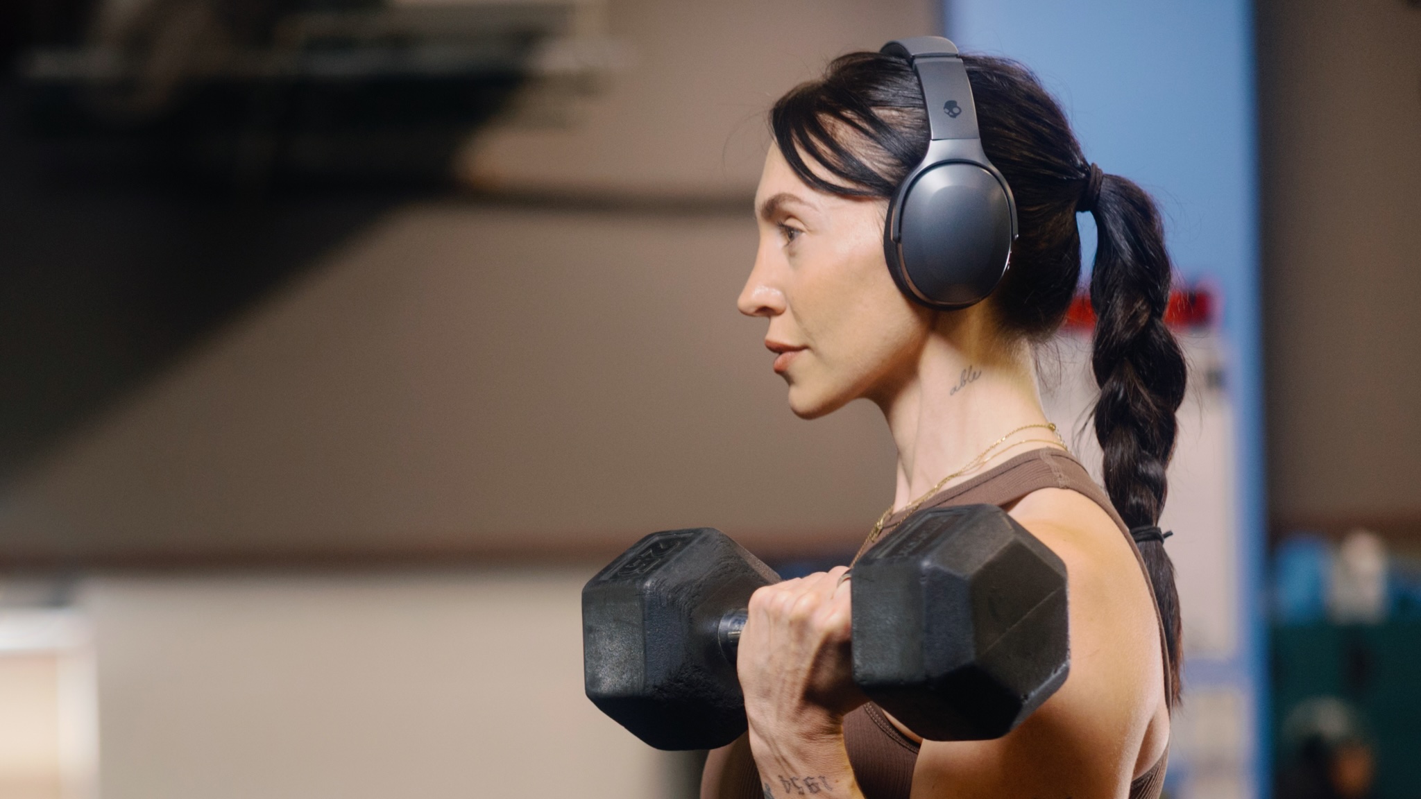 A woman wearing Skullcandy Crusher 540 Active headphones lifting a large weight in the gym