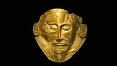 A gold mask of a man's face against a black background