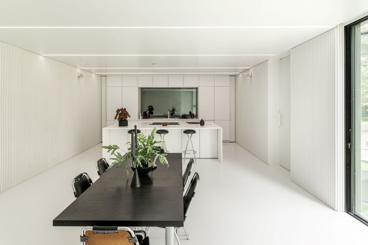 A bright white kitchen-diner with a black wooden table sitting in front of a white kitchen island