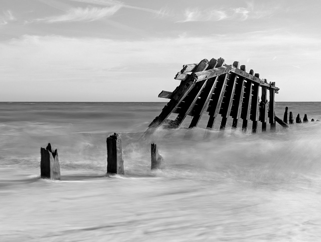 A damaged groyne on a UK beach, the high tide is smashing into it, with the moving water blurred using a long exposure photography technique