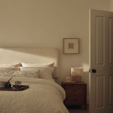 White bedroom with a cream headboard and white bedding, a small picture in an oak frame and a dark wood chest of drawers