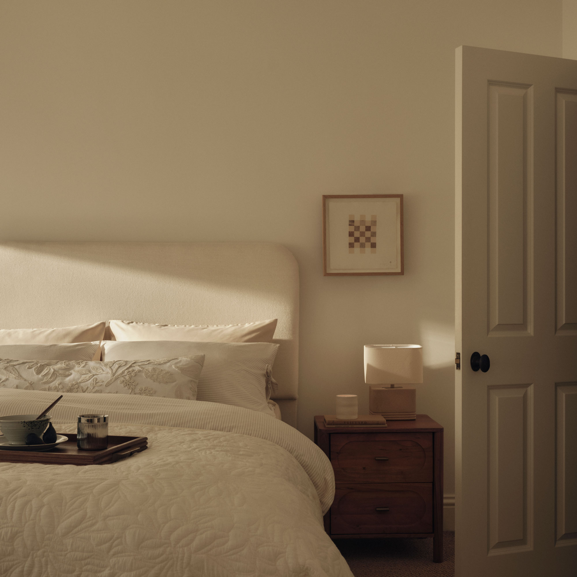 White bedroom with a cream headboard and white bedding, a small picture in an oak frame and a dark wood chest of drawers