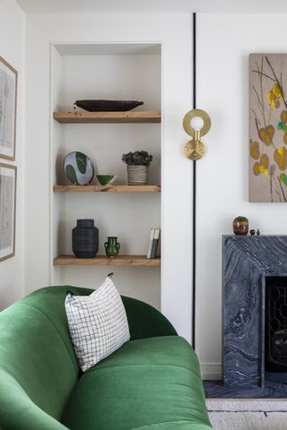 alcove shelving with wooden shelves, green velvet sofa, wall light, marble fireplace