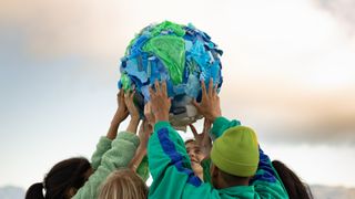 a group of teenagers hold up a model of planet earth made of plastic.