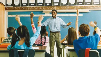 Teacher Standing in Front of a Elementary School Class of Raised Hands