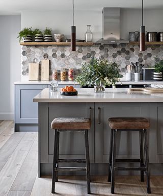 A kitchen with a gray island and gray and white hexagonal wall tiles