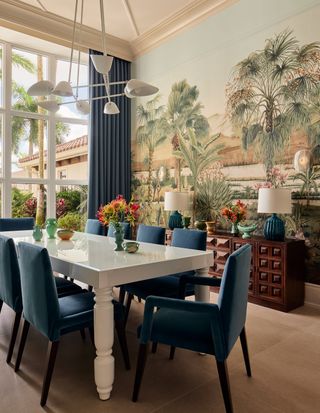 A dining room with a scenic mural on the walls picturing palm trees and a lake