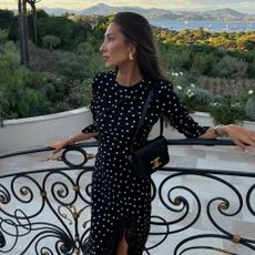 Influencer @fakerstrom wears a long-sleeve polka dot dress with pointed-toe heels, a black bag and large gold earrings.