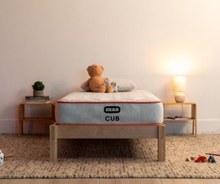 A teddy bear on the Bear Cub Kid's Mattress against a white wall.