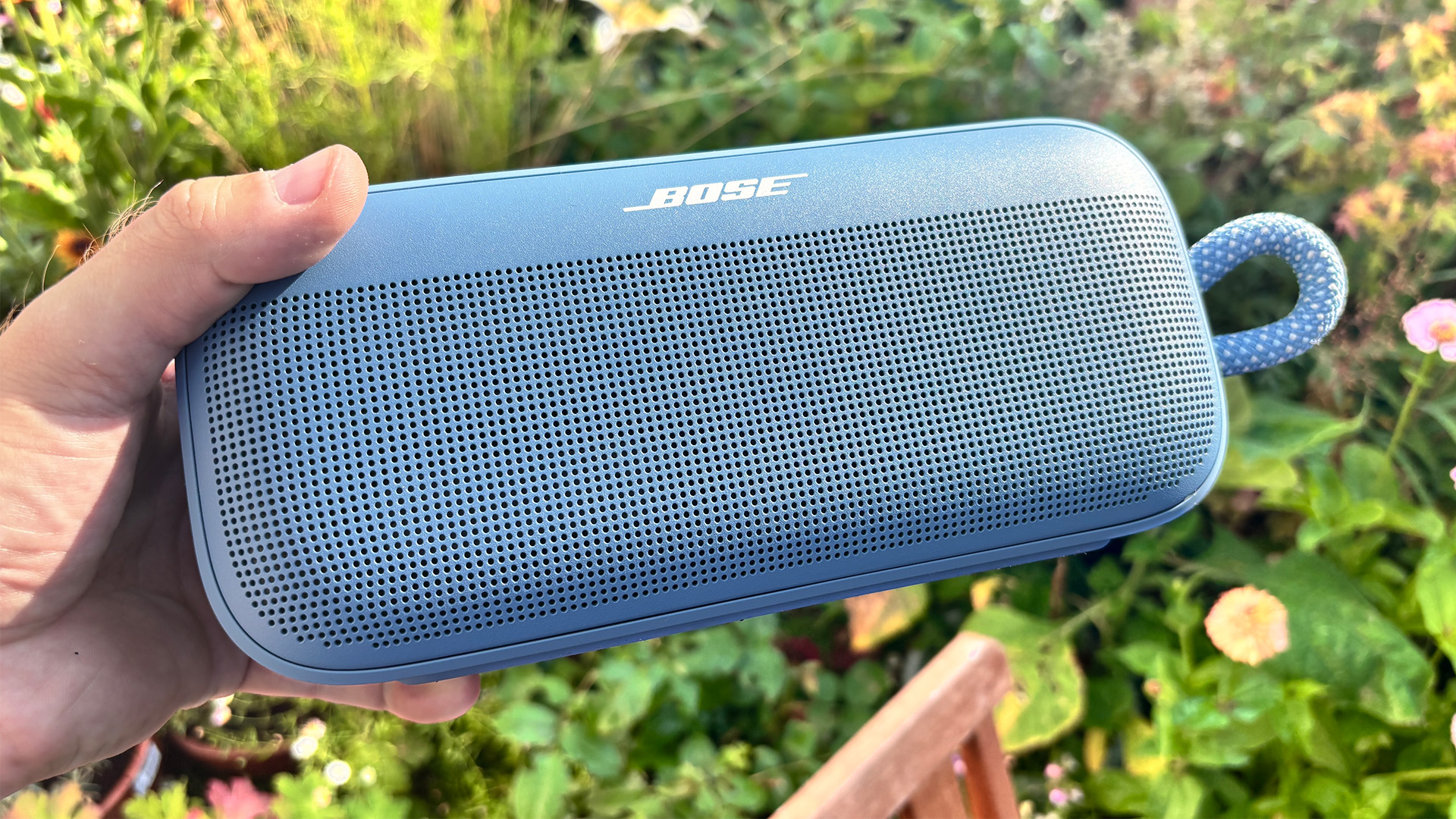Bose SoundLink Plus wireless speaker held in hand in front of flowers