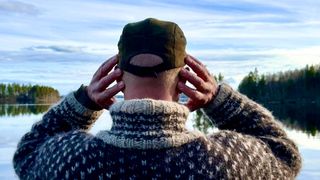 man with hands over ears in front of a lake