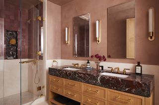 A bathroom with pink walls, a wooden vanity, and a shower with pink tiles