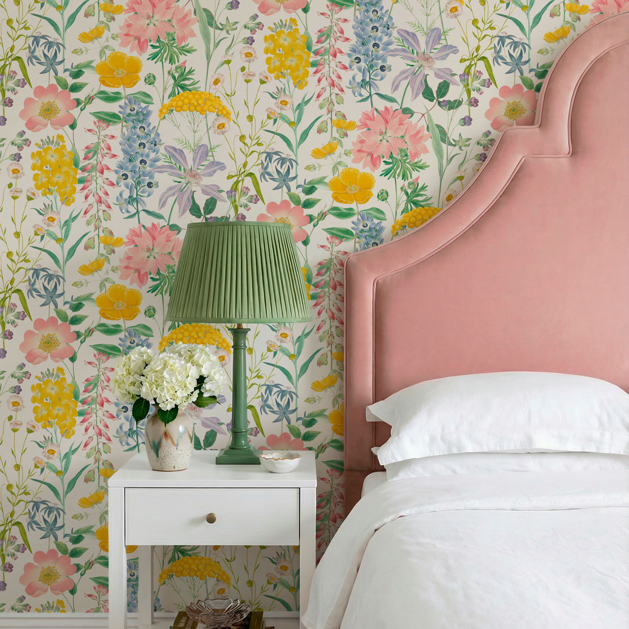 Pink velvet headboard, floral wallpaper, white bedside table, green table lamp