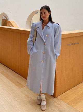 a photo of a woman wearing a long blue coat with pink satin ballet flats