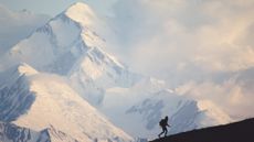 A man hikes in front of a snow-covered mountain in Denali National Park and Preserve in Alaska