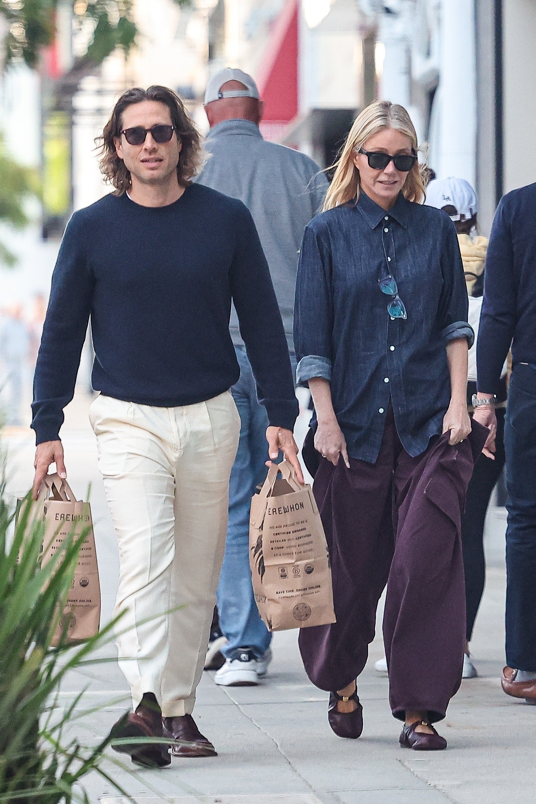 Gwyneth Paltrow walks down the street wearing burgundy trousers with burgundy flats and a denim shirt.