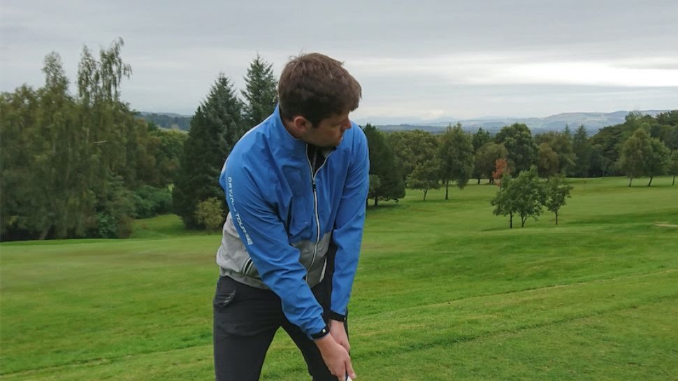 A man wearing a blue waterproof golf jacket while taking a swing