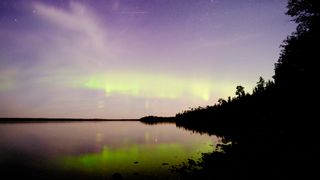 The northern lights reflected over a lake with a Perseid meteor in the frame