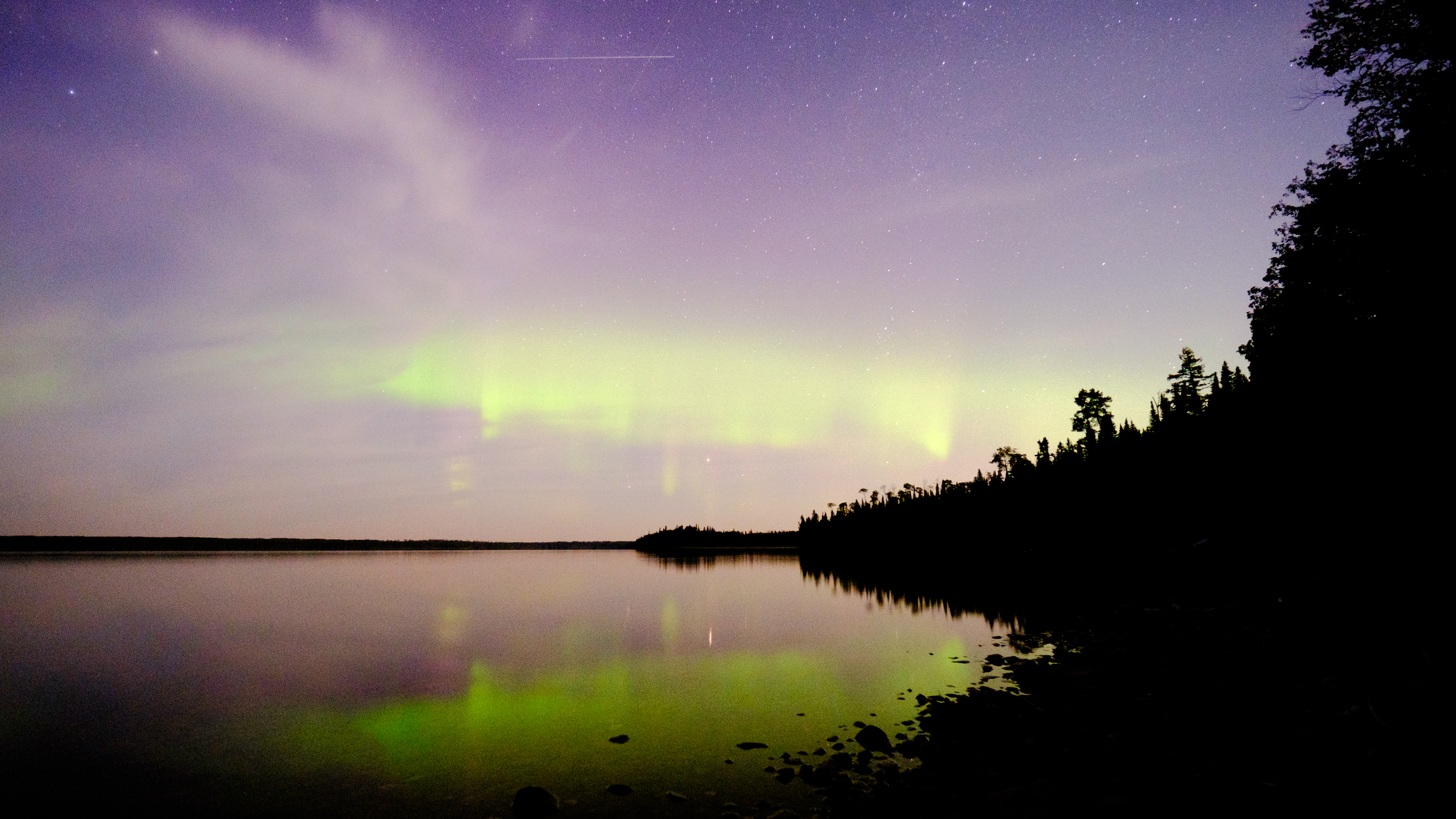 The northern lights reflected over a lake with a Perseid meteor in the frame