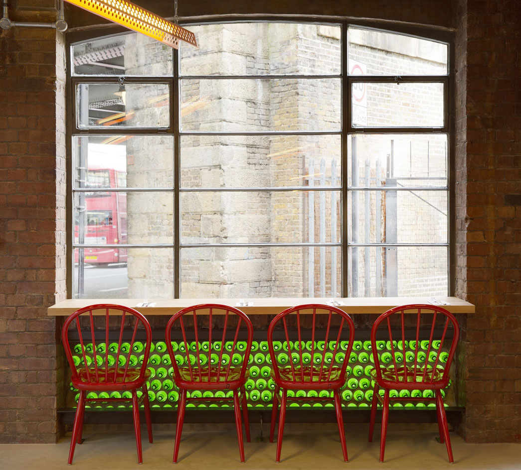 A table with red chairs in front of a large window with a round green pattern on the wall below it.