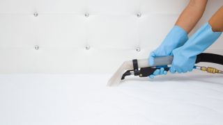 A person wearing blue gloves vacuums the top of a white mattress