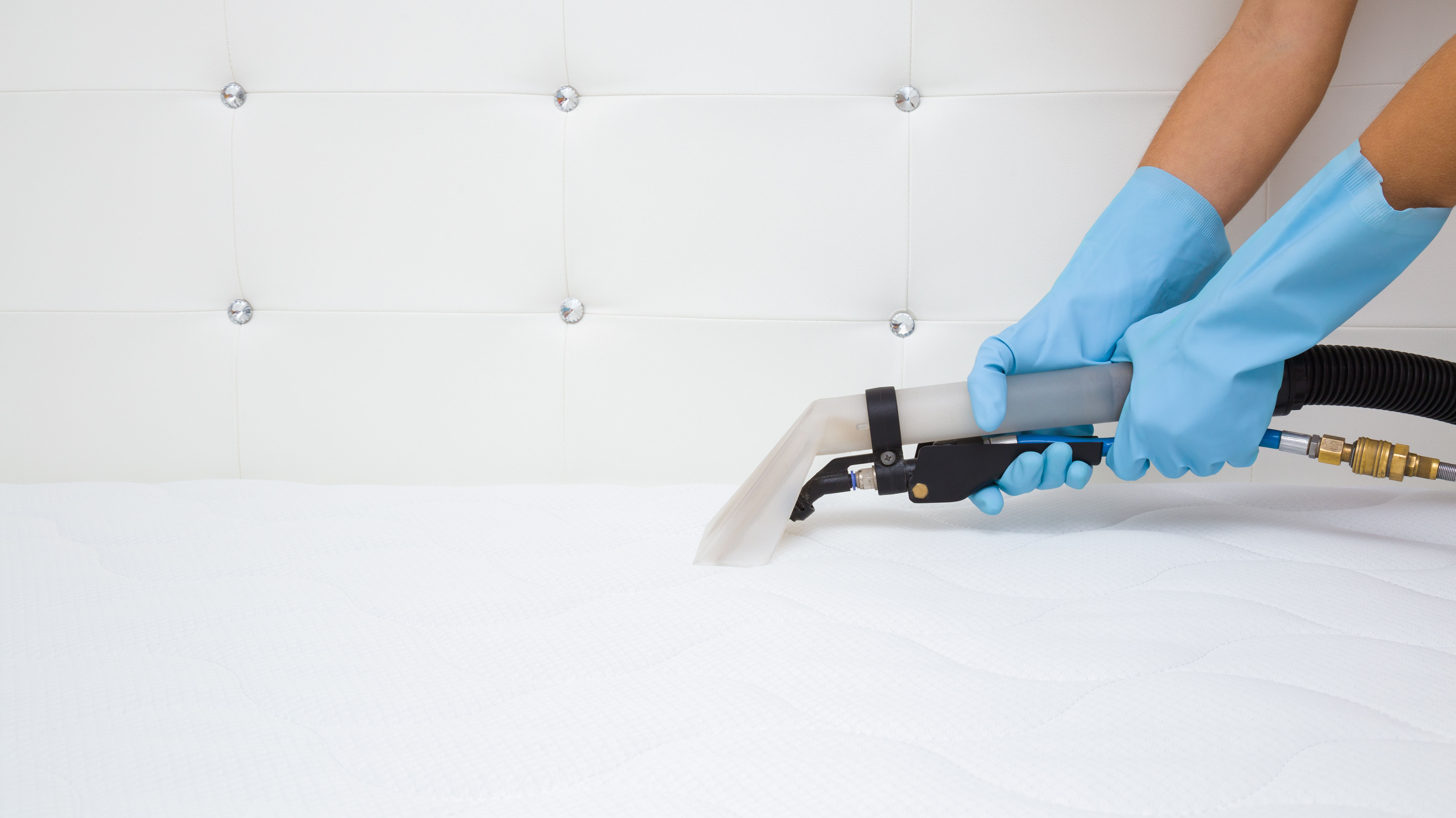 Eine Person mit blauen Handschuhen saugt die Oberseite einer weißen Matratze ab