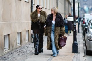 Two women walk down the street at copenhagen fashion week wearing contrasting faux fur coats