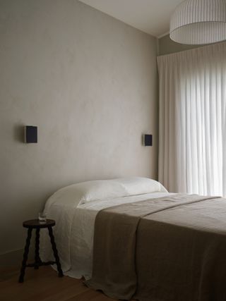 A bedroom with limewash walls, a white and brown bed cover and a white ceiling light