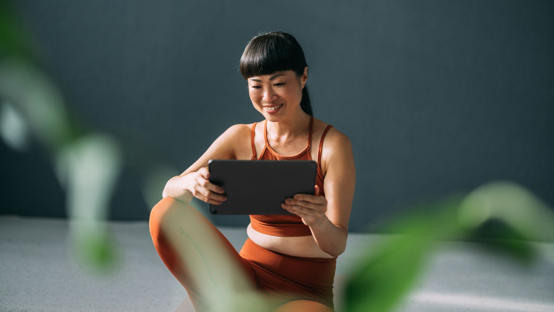 Woman preparing to do tai chi walking wearing activewear and sitting on the floor surrounded by plants