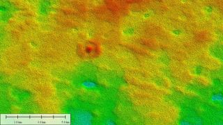 radar image shows a bullseye-shaped mound in a mostly flat landscape; image is shown from above and looks like a heat map with red representing high points and green representing low